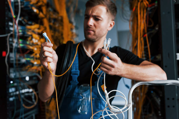 istock Young man in uniform feels confused and looking for a solution with internet equipment and wires in server room 1310873790