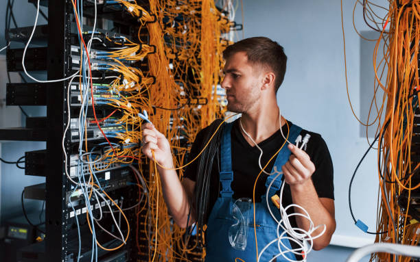istock Young man in uniform feels confused and looking for a solution with internet equipment and wires in server room 1310873950