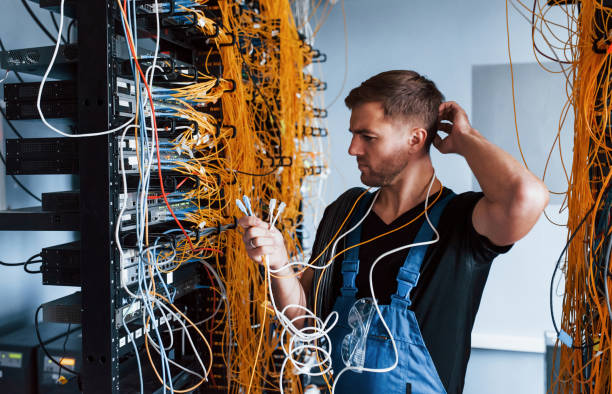 istock Young man in uniform feels confused and looking for a solution with internet equipment and wires in server room 1310874011