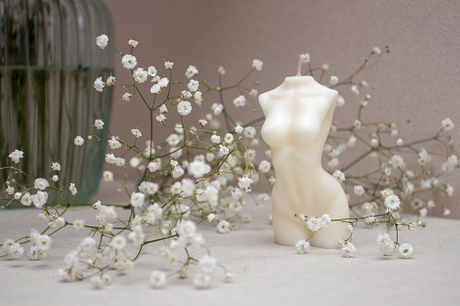 Candle figure of a woman on a table with a vase of white flowers.