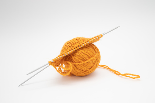 Ball of woolen thread for knitting orange color and knitting needles.