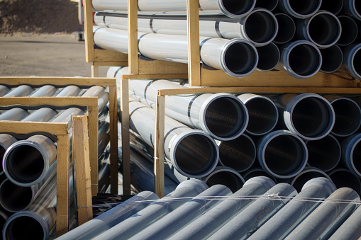 Stack of stored new grey PVC plastic pipes on the construction site