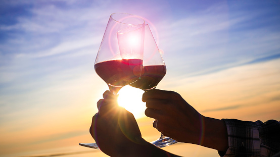 Cheers with wine glasses of couple in a beautiful sunset and lens flare on  beach  background