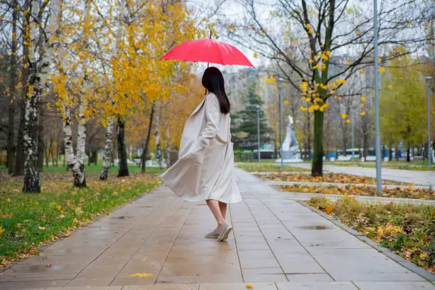 Photo of woman in the park dancing under a red umbrella in the rain