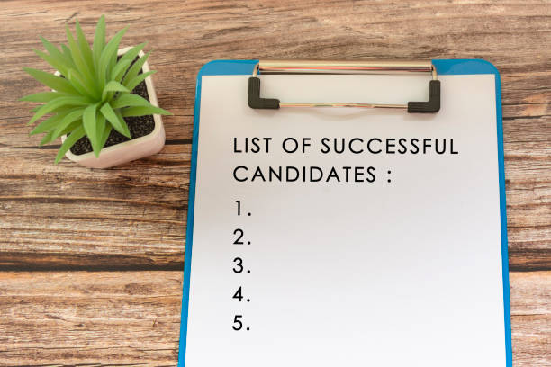 Text on blue clip board with potted plant on wooden desk - List of successful candidates stock photo