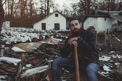 A handsome bearded lumberjack stops at hard work, has to rest while cutting wood and preparing for firewood.