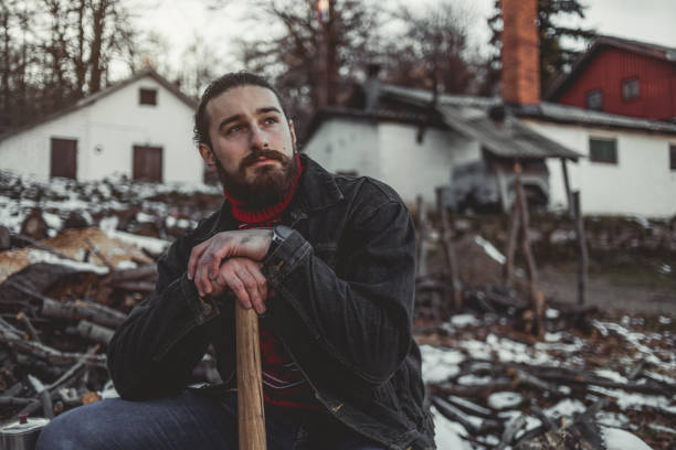 A handsome bearded lumberjack stops at hard work, has to rest while cutting wood and preparing for firewood.