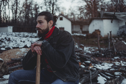 A handsome bearded lumberjack stops at hard work, has to rest while cutting wood and preparing for firewood.