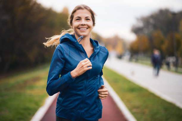 Sporty woman Beautiful adult woman is jogging outdoor on cloudy day in autumn. all weather running track stock pictures, royalty-free photos & images