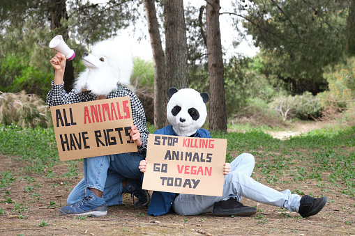 Activist protesters wearing animal masks shouting through a bullhorn to highlight cruelty and promote vegan lifestyle. Animal rights protest in a forest.