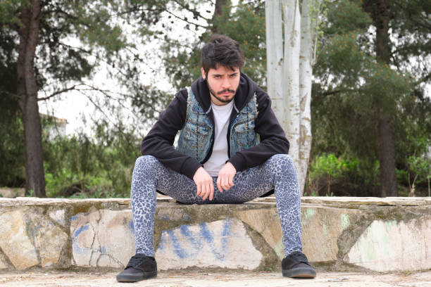 Portrait of a young punk man wearing leopard leggins, black hoody and denim vest. Millennial generation. Portrait of a young punk man wearing leopard leggins, black hoody and denim vest. Millennial generation. emo boy stock pictures, royalty-free photos & images