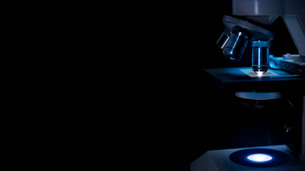 microscópio em trabalho de parto em luz azul escuro e fundo preto. - microscope medical exam healthcare and medicine science - fotografias e filmes do acervo