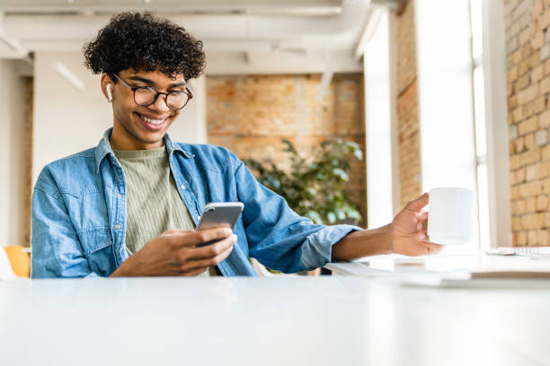 istock Confident smiling young afro businessman drinking coffee and using phone in office 1310895962
