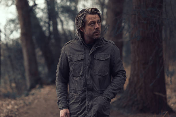 istock Blonde man in a green coat walks on a forest path. 1310895992