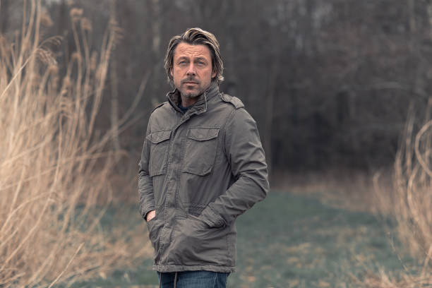 istock Blond man in green jacket on grassy path between tall reed in nature reserve. 1310896025