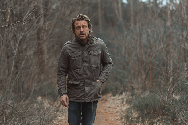 istock Blond man in green coat walks on a pathway between trees in nature reserve. 1310896068
