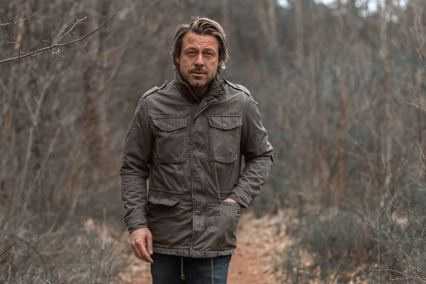 istock Blond man in green coat walks on a pathway between trees in nature reserve. 1310896075