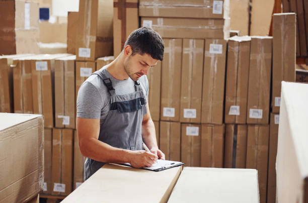 istock Young male worker in uniform is in the warehouse with notepad and pen 1310901861