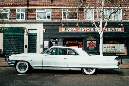 London, UK - 1 April, 2021: an old vintage white Cadillac car parked on a residential city street in London, UK.