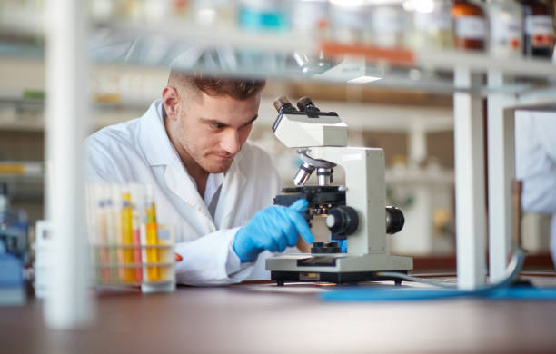 um jovem estudante de química ajusta um microscópio em um laboratório. ciência, química, laboratório, pessoas - genetic research men chemical protective glove - fotografias e filmes do acervo