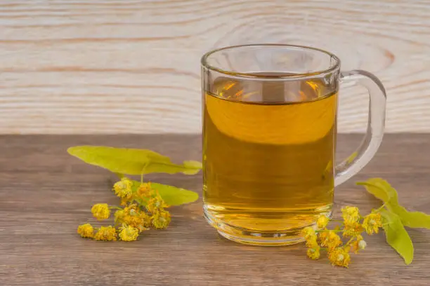 herbal tea in transparent glass mug with fresh linden flowers on wooden table