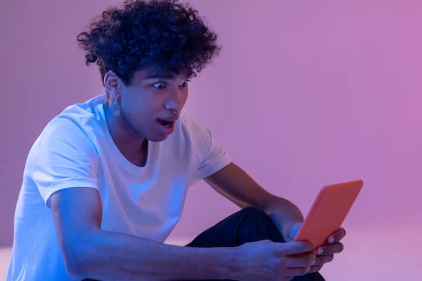 istock Curly-haired young guy holding a tablet and looking shocked 1310911321