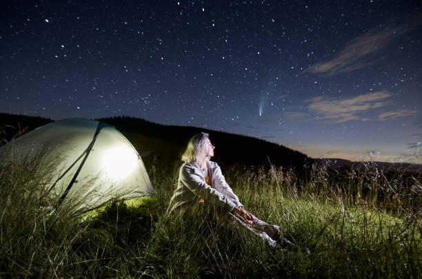istock Beautiful young woman sitting on grass under night starry sky. 1310912136