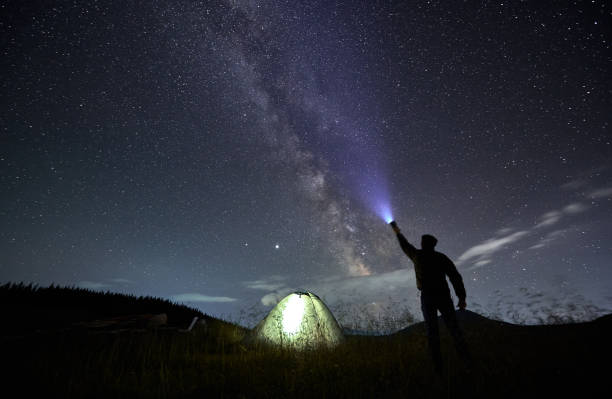 istock Male traveler shining flashlight into night starry sky. 1310912138