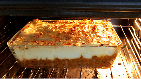 Stock photo showing a cottage / shepherd's pie with crispy golden, mashed potato topping, placed to bake in a hot oven in a glass dish.