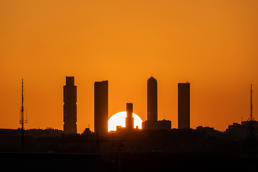 Silhouette of Madrid skyline with its five towers while the sun sets behind the skyscrapers.