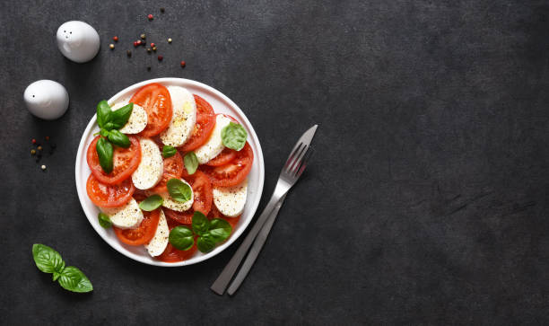 caprese est un apéritif tomate et mozzarella. salade italienne traditionnelle sur un fond noir avec l’espace pour le texte. vue d’en haut. - cutting plate photos et images de collection