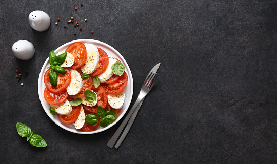 Caprese is a tomato and mozzarella appetizer. Traditional Italian salad on a black background with space for text. View from above.