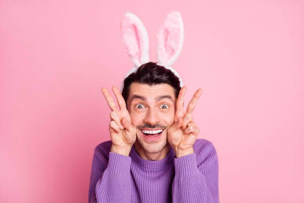 istock Photo of charming funky young man dressed purple pullover rabbit ears showing v-signs cheeks isolated pink color background 1310920470