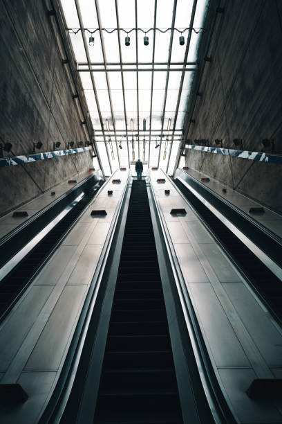 Wide angle image of an ultra modern subway station in the city of London, with one man in silhouette on the elevator taking him up to the city street or to the subway station platforms below.