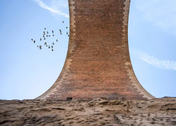 Photo of Old railway arch viaduct bridge made of stone and brick looking up from ground high above in the blue sky. Birds taking off from train rail viaducts pigeons flying over arches.