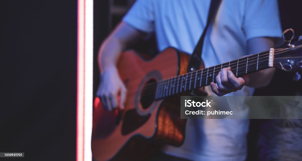 Close up of a guitarist playing an acoustic guitar in a dark room copy space. A man plays an acoustic guitar in a room copy space. Live performance, acoustic concert, practice. 30-34 Years Stock Photo