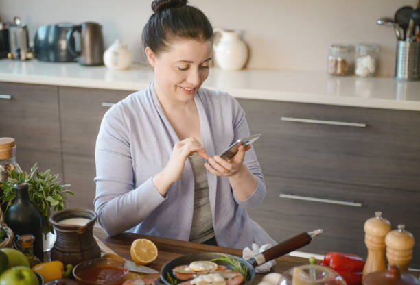 istock woman cooking in the kitchen ( with fish salmon, smart phone) 1310931903