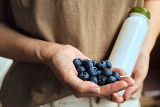 bleuets et une bouteille de yogourt dans les mains d’une femme. baies biologiques naturelles. les bleuets frais se ferment vers le haut. délicieuse baies d’été. une bonne nutrition. baies pour le dessert. sain - blueberry picking freshness berry photos et images de collection