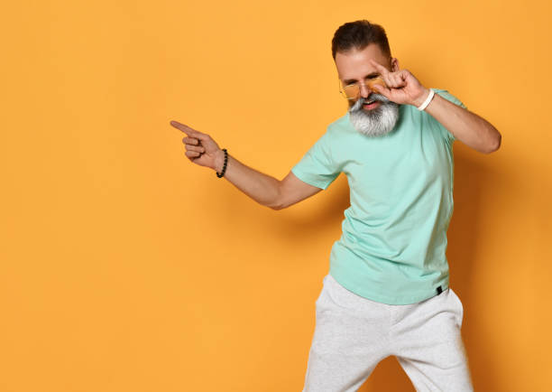 Stylish trendy gray-haired hipster guy dancing and having fun on bright orange background