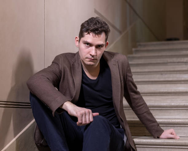 istock Young man sits indoor on the stairs looking at camera 1310936222
