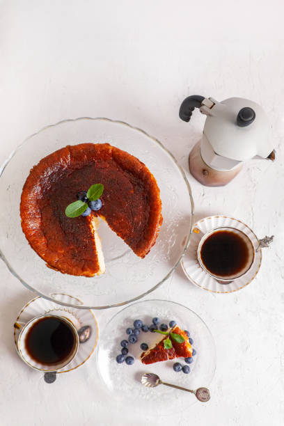istock Homemade Basque burnt cheesecake on a plate with blueberries and mint leaves on light background,with cop of coffie and geyser coffee maker flat lay top view 1310936237