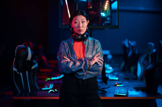 giovane giocatore asiatico in un auricolare posa per la fotocamera con le braccia conserte - gaming systems foto e immagini stock