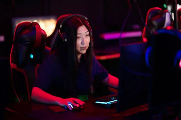 Photo of A close-up portrait of a gamer girl wearing headphones in a computer club while playing a game
