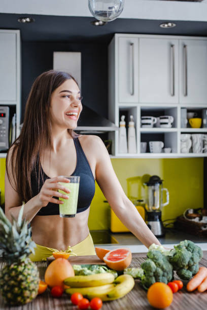 atletyczna młoda kobieta w odzieży sportowej sprawia, że ciesz się zdrowym napojem w domu - vegan food cheerful vertical indoors zdjęcia i obrazy z banku zdjęć