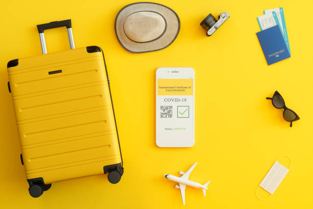 digital covid-19 vaccine passport app na ekranie telefonu komórkowego. paszport, bilety lotnicze, żółta walizka i ochronna maska na twarzy z żółtym tłem. - hand held shot zdjęcia i obrazy z banku zdjęć