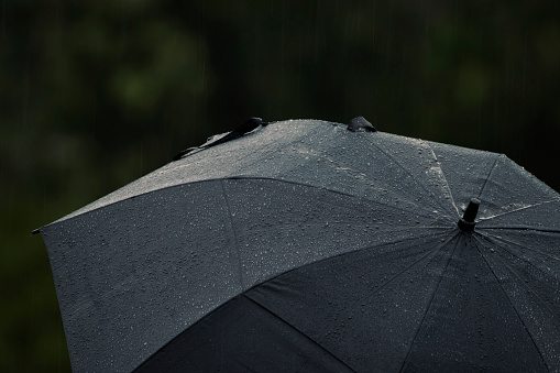 Dark and gloomy, raindrops falling on umbrella. Wet weather concept.