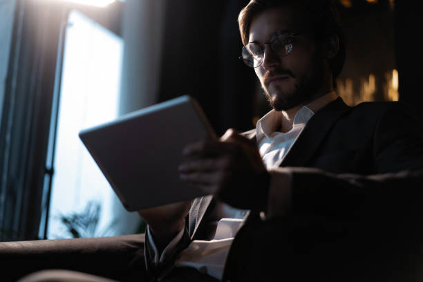 istock Businessman working using tablet computer while sitting in cafe late at night in front of windows overlooking the city. 1310949077