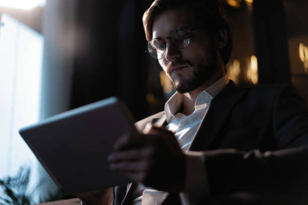 istock Businessman working using tablet computer while sitting in cafe late at night in front of windows overlooking the city. 1310949359