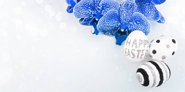 istock Composition of glitter inscription Happy Easter on a white egg and shining bokeh on a gray background. Blue orchid, eggs with black and silver lines and polka dots. Flat lay, top view, copy space 1310952201
