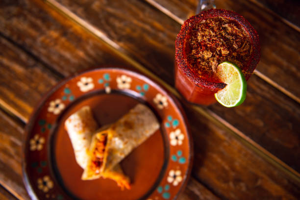 Mexican burrito and michelada beer with tomato juice with copy space. Michelada beer with tomato juice and burritos. Mexican food on wooden table. Concept of traditional food and mexican drink.